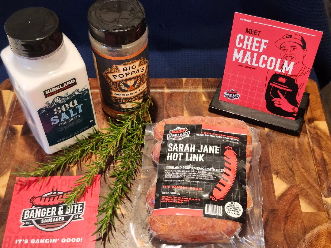 Cutting board display showcasing seasonings, a postcard with an illustrator of the owner, Malcolm, a square thank you card, and a "Sarah Jane Hot Link" sausage pack